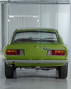 an old green car is parked in a parking garage with its hood up and the back lights on