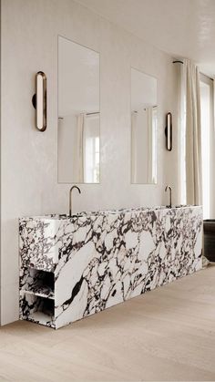 a white and black bathroom with marble counter tops, mirrors and lights on the wall