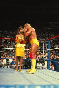 two women in yellow outfits standing next to each other on a wrestling ring with spectators watching