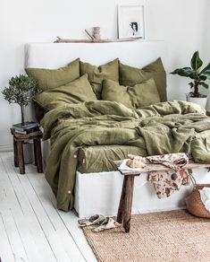 a bed with green sheets and pillows in a white room next to a potted plant