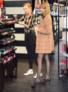 two women are standing in a store looking at their cell phones and one is wearing tights