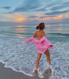 a woman in a pink dress is walking into the water at sunset on the beach