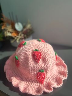 a crocheted pink hat with strawberries on the brim sits on a table