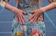 a woman with her hands on the back of her jean overalls that has flowers all over it