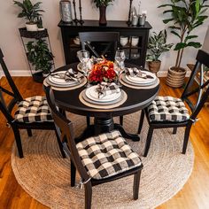 a dining room table set for four with black and white checkered chairs, place settings and potted plants