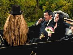 two people in a horse drawn carriage, one with long hair and the other wearing a top hat
