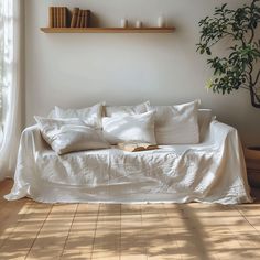 a bed with white sheets and pillows in a room next to a potted plant