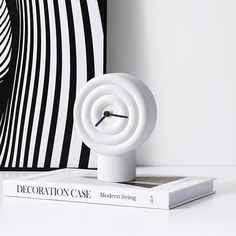 a white clock sitting on top of a book next to a black and white wall