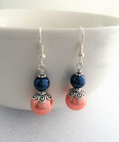 two pairs of earrings with coral and blue beads on white surface next to bowl full of water