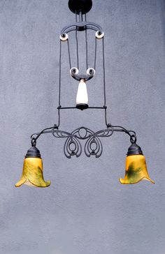 three lights hanging from the ceiling in front of a gray wall with two yellow and white shades