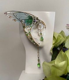 This Pair of Handcrafted Ear wraps with Wings has been created using Brass Wires, and Peridot Swarovski Crystals. They are Comfortable and easy to wear with a Hoop on the back making it easy to adjust; Perfect for any Festive event, Cosplay, or night out on the Town. All Items are made to order. If you have something Special in mind… Please Contact us… We Love Custom Orders. Enchanted Forest Accessories, Cicada Wings Open, Rainbow Ear Piercings, Fairy Ears Aesthetic, Fae Jewelry, Forest Fairy Wings, Fairytale Accessories, Fae Wings, Mythical Jewelry