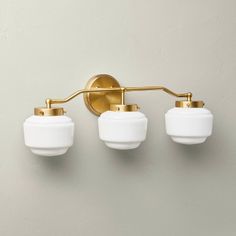 three light bathroom fixture with white glass shades and brass finish on the wall behind it