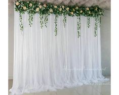 white sheer curtains with flowers and greenery hanging from the ceiling in front of a wall
