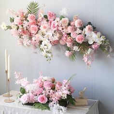 pink and white flowers are arranged on a table next to a wall with two candles