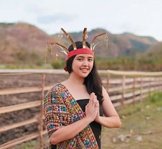 a woman wearing a headdress standing in front of a fence with her hands clasped