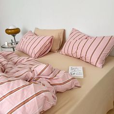 a bed covered in pink and brown striped sheets with two pillows on top of it