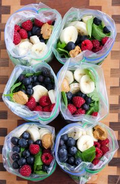 four plastic bags filled with fruit and veggies on top of a wooden table