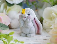 a white stuffed animal with a yellow bow on it's head sitting in front of flowers