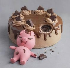 a pink pig next to a chocolate cake with icing and chocolate decorations on it