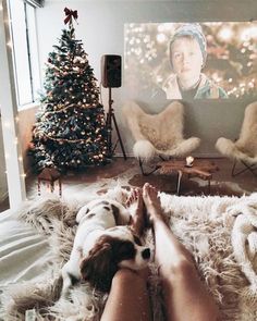 a woman laying on top of a fluffy rug next to a christmas tree and a tv