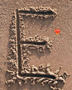 the word e is written in the sand with a red heart on it's side