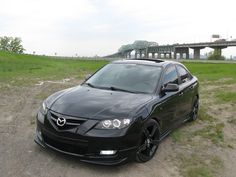 a black car is parked on the side of the road near a bridge and grassy area