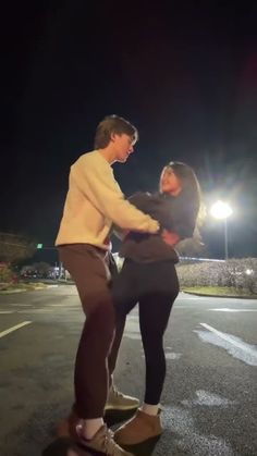 a man and woman standing on top of a skateboard in the middle of an empty parking lot