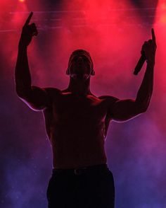 a shirtless man holding two microphones in front of red and blue lights on stage