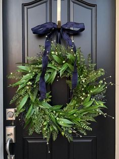 a wreath with blue ribbon hanging on the front door to a house that is decorated with greenery