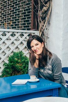 a woman sitting at a blue table with a coffee cup in her hand and smiling