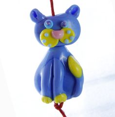 a blue and yellow bear ornament hanging from a red string on a white background