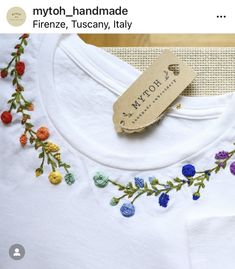a white t - shirt with flowers on it and a tag hanging from the front