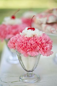 pink carnations and white daisies in a glass vase on a table with other plates