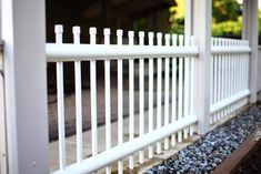 a white picket fence sitting next to a gravel covered ground with rocks on the ground