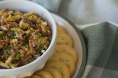 a white bowl filled with food sitting on top of a plate next to crackers