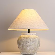 a white lamp sitting on top of a table next to a gray wall behind it