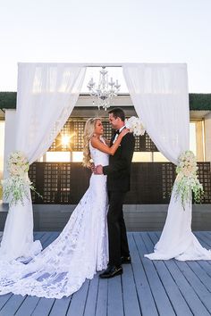 a bride and groom standing in front of a white wedding arch with chandelier