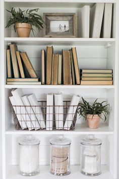 some books are sitting on top of a book shelf next to two glass jars with plants in them