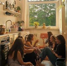 four young women sitting on the floor drinking wine in a small kitchen with an open window