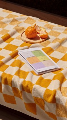a yellow and white checkered table cloth with an orange on it next to a book