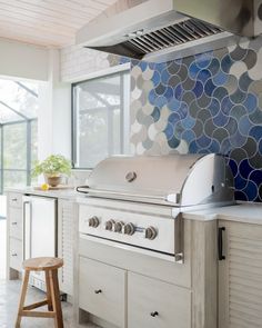 an outdoor kitchen with white cabinets and blue tiles on the backsplash, along with stools