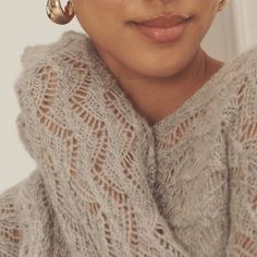 a close up of a woman wearing large gold hoop earrings and a white knitted sweater