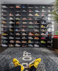 someone's feet on the floor in front of a large display of tennis shoes