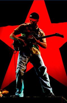 a man with a guitar on stage in front of a red star and black background