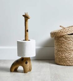 a giraffe shaped toilet paper holder next to a roped basket on the floor