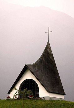 a church with a steeple and a cross on it's roof in the mountains