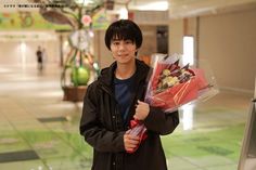 a young man is holding flowers in his hand and smiling at the camera while standing next to an escalator