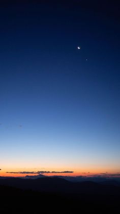 the moon and venus are seen in the sky at sunset over some distant landforms