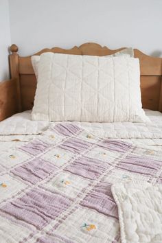 a bed with white and purple bedspread on top of it next to a wooden headboard