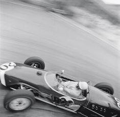 a black and white photo of a man driving a race car down a hill side